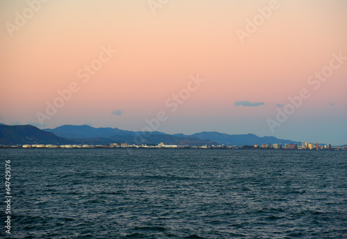 Coastline on sunset. Mediterranean sea at Alboraya beach and Port Saplaya in Valencia. Waves at sea on sunset. Seaside Spain beach on sunrise. Coastline in evening time. Shore on mountains landscape.