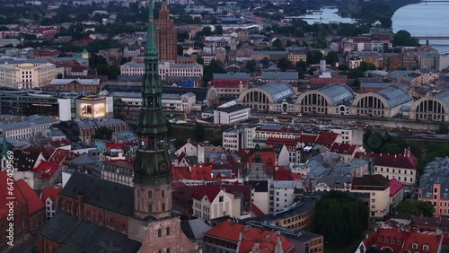 Aerial cinematic footage of historic city centre with tall church tower. Pavilions of large Riga Central Market and other tourist sights at dusk. Riga, Latvia