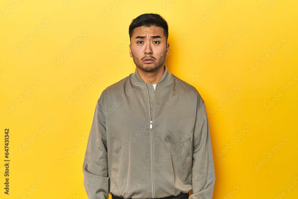 Obraz premium Stylish Asian man in gray jacket on yellow studio sad, serious face, feeling miserable and displeased.