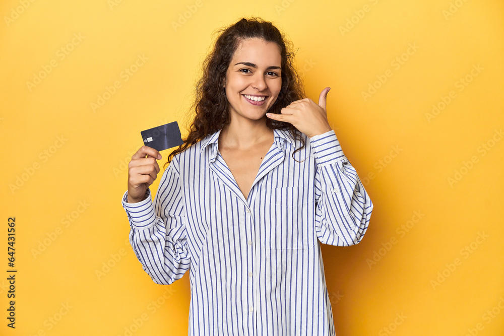 Woman holding a credit card, yellow backdrop, showing a mobile phone call gesture with fingers. Woman holding a credit card, yellow backdrop, showing a mobile phone call gesture with fingers.