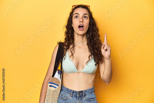 Woman in summer look, bikini, beach essentials, pointing upside with opened mouth. photo