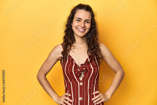 Young Caucasian woman, yellow studio background, confident keeping hands on hips.