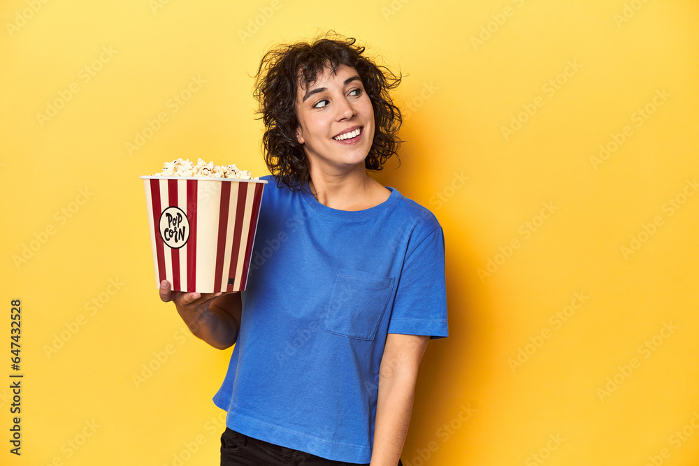 Curly-haired woman with popcorn for movie, studio looks aside smiling, cheerful and pleasant. Curly-haired woman with popcorn for movie, studio looks aside smiling, cheerful and pleasant.