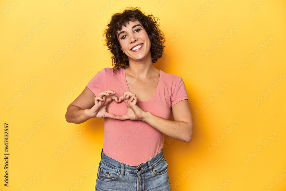 Curly-haired Caucasian woman in pink t-shirt smiling and showing a heart shape with hands. Curly-haired Caucasian woman in pink t-shirt smiling and showing a heart shape with hands.