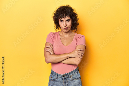 Curly-haired Caucasian woman in pink t-shirt frowning face in displeasure, keeps arms folded. © Asier