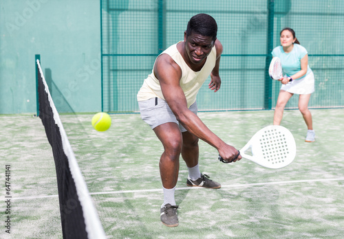 African american man and his female partner playing paddle tennis on the padel court © JackF