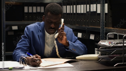 In incident room, police officer answers landline phone, getting fresh case information and forensic evidence report in order to apprehend culprit. Private investigator on phone with a criminologist.