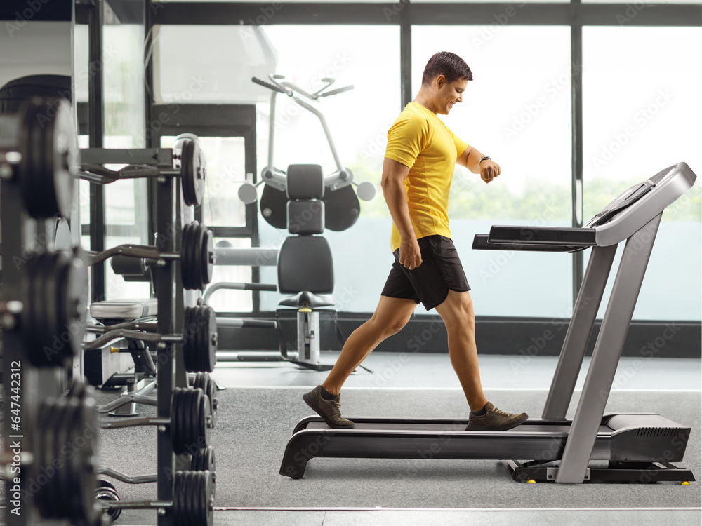 Fototapeta premium Man in sportswear walking on a treadmill and looking at his smartwatch