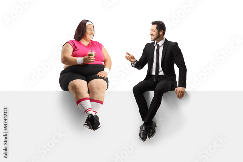 Businessman talking to a corpulent woman seated on a blank panel and holding a healthy green smoothie
