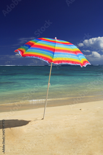 Colorful Beach Umbrella On The Shoreline Of A Tropical Beach, Calm Water Lapping On The Shore. photo