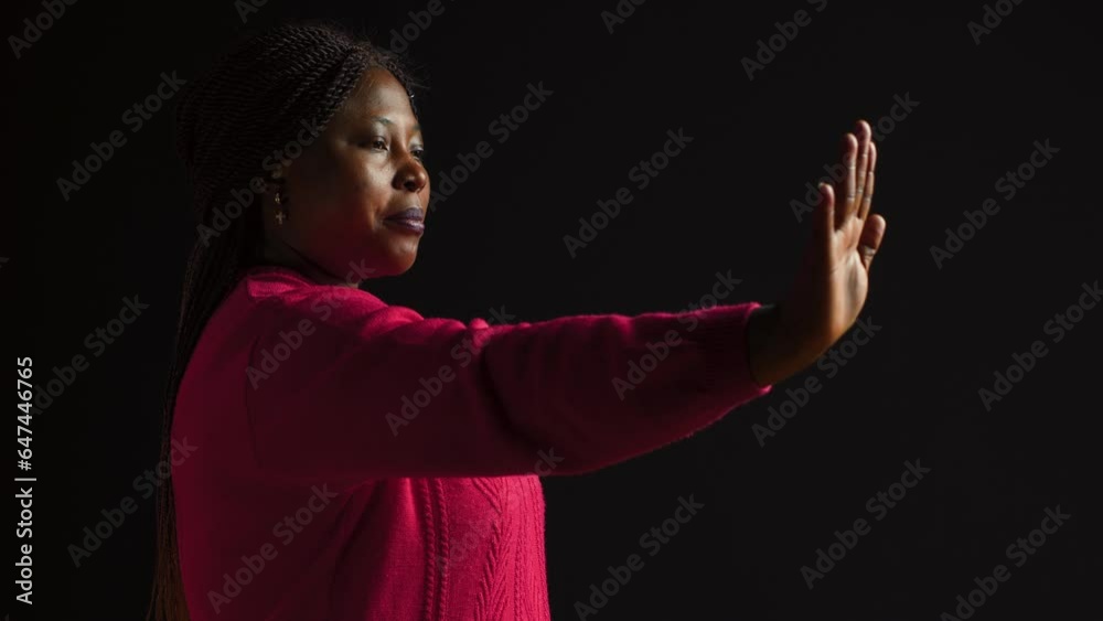 African american woman firmly signals stop using hand gesture in isolated black background. Female fashion model expresses disapproval rejecting and disagreeing in side-view portrait shot.