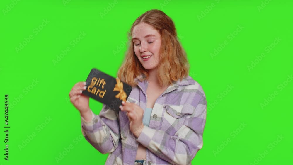 Happy caucasian woman showing pointing on gift discount certificate voucher coupon for store holidays sale. Redhead girl with shopping christmas surprise card isolated on green chroma key background Happy caucasian woman showing pointing on gift discount certificate voucher coupon for store holidays sale. Redhead girl with shopping christmas surprise card isolated on green chroma key background
