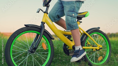 Little boy rides bike in park on green grass. Happy family in park. Childs feet are pedaling. Boy rides bike in summer, pedaling. Childhood dream to travel. Sports lifestyle of child, boy cyclist play