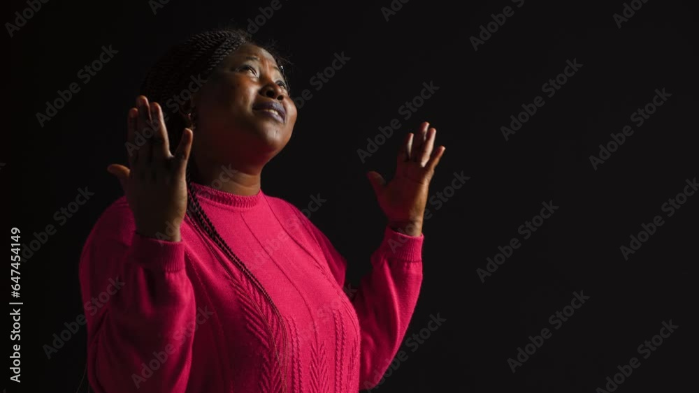 Graceful black woman gazing upwards with palms extended in gesture of reverance and adoration. Side-view portrait of african american lady engaged in prayerful reflection in isolated background.