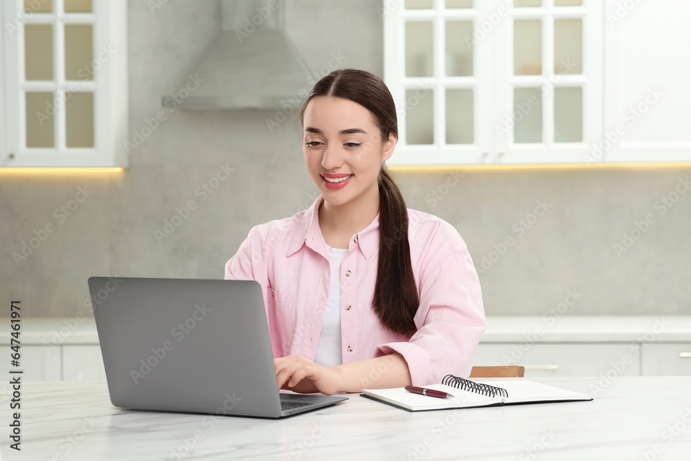 Woman using laptop at white table in kitchen Woman using laptop at white table in kitchen