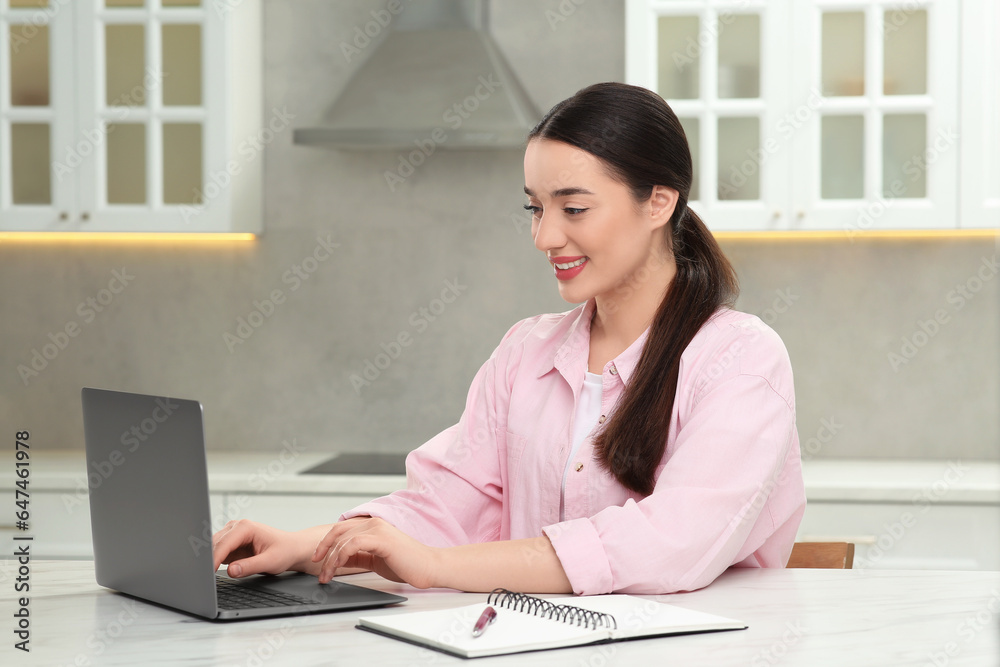 Woman using laptop at white table in kitchen Woman using laptop at white table in kitchen