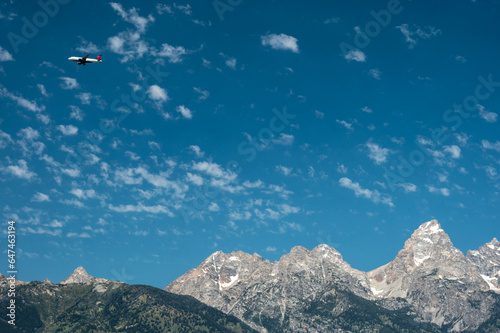 Delta Jet Flies Over The Grand Tetons Against Blue Sky With Thin Clouds