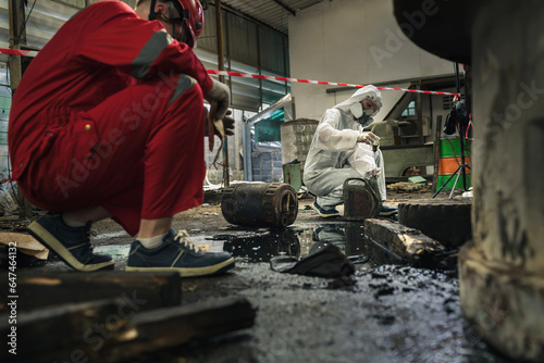 Male and female workers or scientists wearing red safety suits and gas masks undergoes cleaning and mopping up of spilled oil in the factory area for inspection in the laboratory. photo