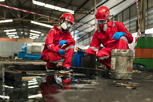 Male and female workers or scientists wearing red safety suits and gas masks undergoes cleaning and mopping up of spilled oil in the factory area for inspection in the laboratory.