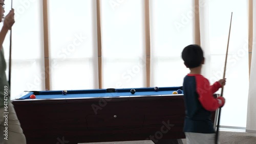 Asian child boy playing billiard or snooker with father. Kid concentrate on cue stick to strike cue ball to pot other balls to pocket. Concept of family sport game, leaning, leisure, goal. photo