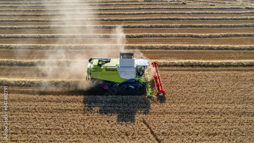 Aerial shot of harvester machinery collecting wheat grain in hot season in rural cultivated golden fields