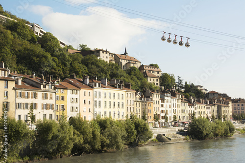 Bubble Gondola Passing Over Old Buildings Along A River; Grenoble, France