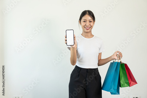 Asian woman holding a credit card Smartphone with white screen and shopping bags, white background, online banking transaction concept in online shopping