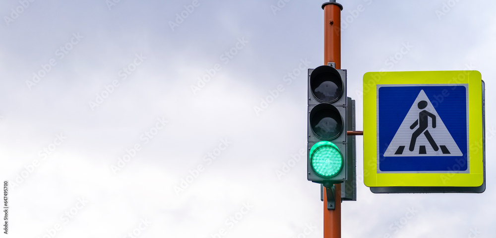 A pedestrian crossing sign with a reflective coating and a traffic light is installed on the street next to the school and warns drivers about the pedestrian crossing. Be careful on the road A pedestrian crossing sign with a reflective coating and a traffic light is installed on the street next to the school and warns drivers about the pedestrian crossing. Be careful on the road
