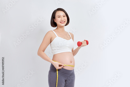 young pregnant woman doing fitness and measuring belly with measuring tape