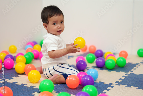 happy infant baby playing colorful balls in playpen