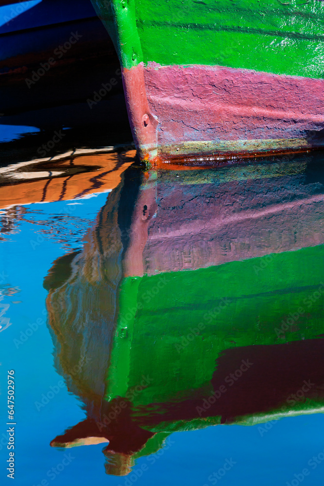 Detail of a small, wooden fishing boat moored to the shore with a mirror image reflection in the calm water in the coastal town of Getaria; Getaria, Gipuzkoa, Spain Detail of a small, wooden fishing boat moored to the shore with a mirror image reflection in the calm water in the coastal town of Getaria; Getaria, Gipuzkoa, Spain