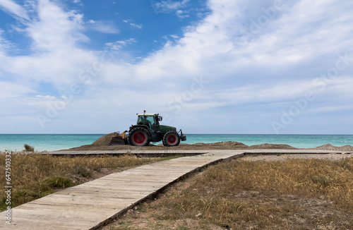 Clining beach and maintenance. Tractor grooming sand on beach shore in Almarda, Spain. Getting beach ready for summer vacation season. Beach grooming machinery. photo