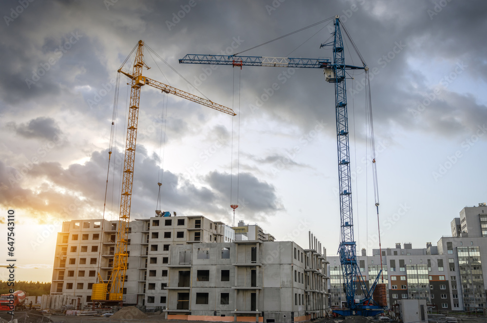 Cranes and buildings under construction against the cloudy sunset sky