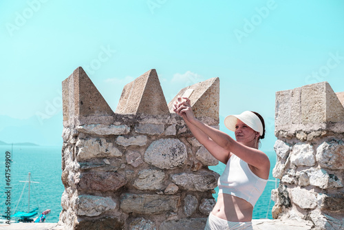 young woman taking selfy on mobile phone on top of ancient castle open air, when travelling historical places photo