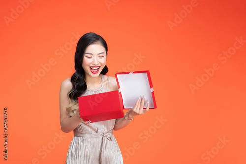 Portrait of a happy smiling girl opening a gift box isolated over red background