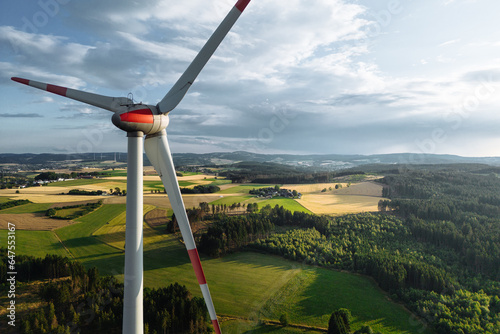 Wind turbines in a hilly forest in front of a partly cloudy, but sunny sky are seen from an aerial view during sunset photo