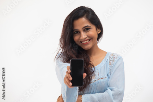 A YOUNG WOMAN SMILING AT CAMERA AND SHOWING HER MOBILE PHONE  photo