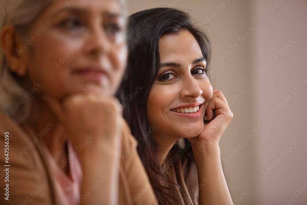 A YOUNG WOMAN SITTING AND SMILING WITH MOTHER SITTING NEAR AND THINKING A YOUNG WOMAN SITTING AND SMILING WITH MOTHER SITTING NEAR AND THINKING