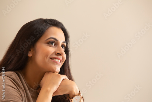 PORTRAIT OF A YOUNG WOMAN SITTING WITH HANDS RESTING ON CHIN AND SMILING photo