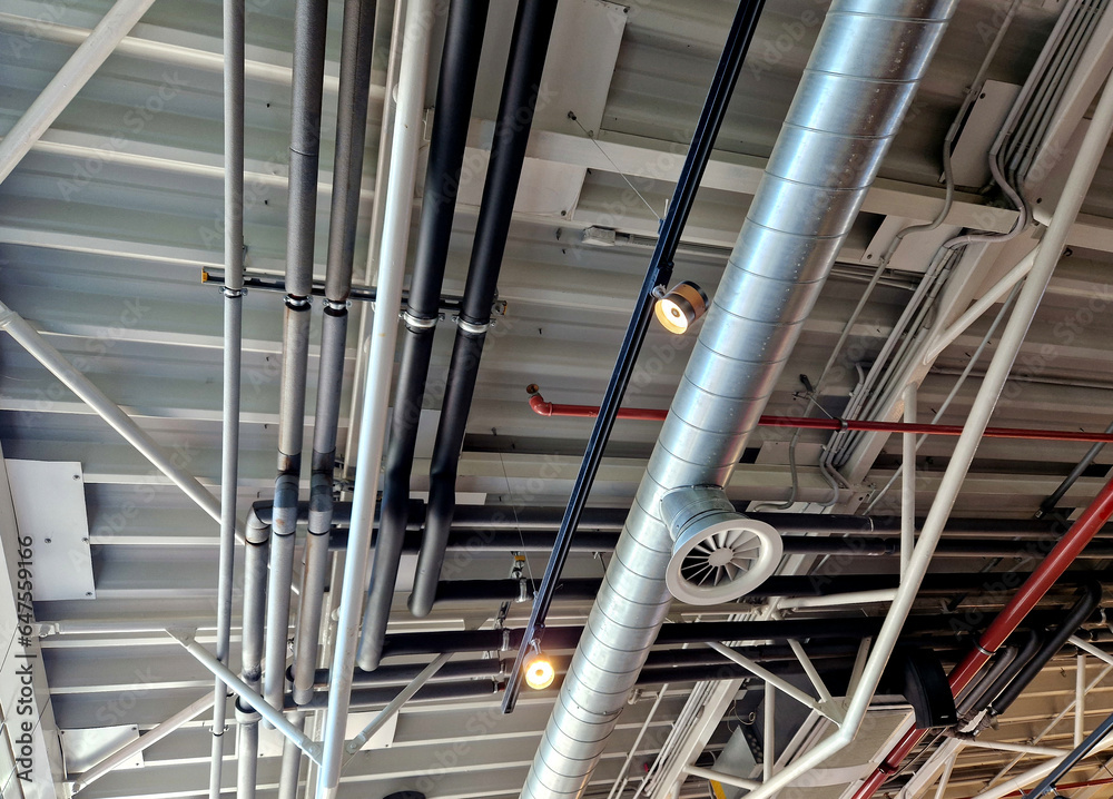 the air handling unit is on the ceiling of the building and is visibly left uncovered. the lights and pipes running under the tin roof give it an industrial feel. whire