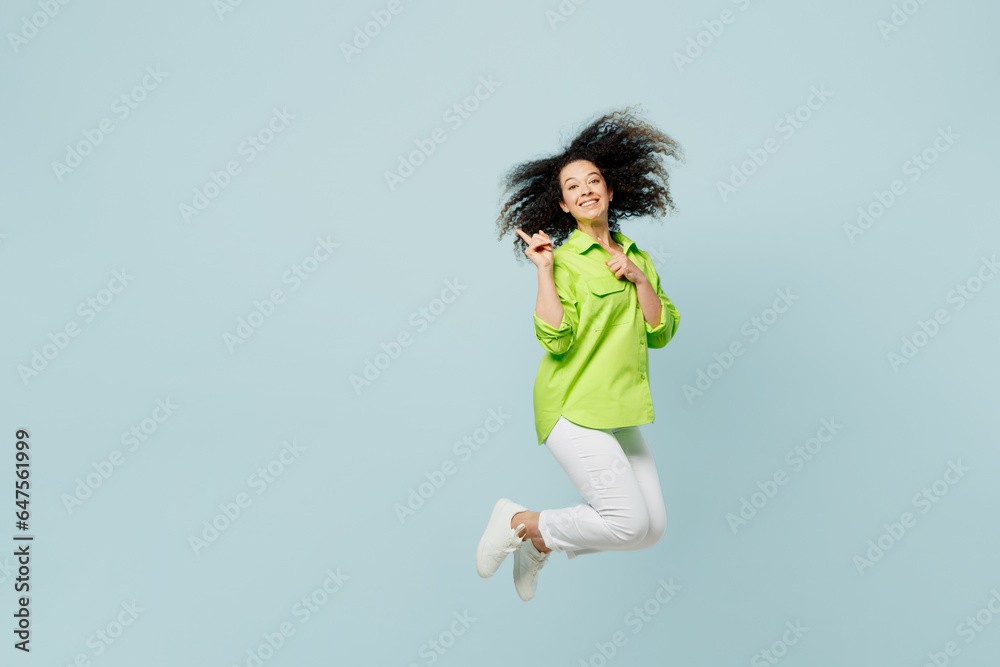 Full body young latin woman she wears green shirt casual clothes jump high point indicate on workspace area copy space mock up isolated on plain pastel light blue cyan background. Lifestyle concept. Full body young latin woman she wears green shirt casual clothes jump high point indicate on workspace area copy space mock up isolated on plain pastel light blue cyan background. Lifestyle concept.