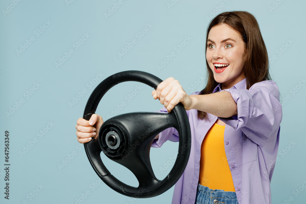 Side view young happy smiling confident woman wears purple shirt yellow t-shirt casual clothes hold steering wheel driving car isolated on plain pastel light blue background studio. Lifestyle concept. Side view young happy smiling confident woman wears purple shirt yellow t-shirt casual clothes hold steering wheel driving car isolated on plain pastel light blue background studio. Lifestyle concept.