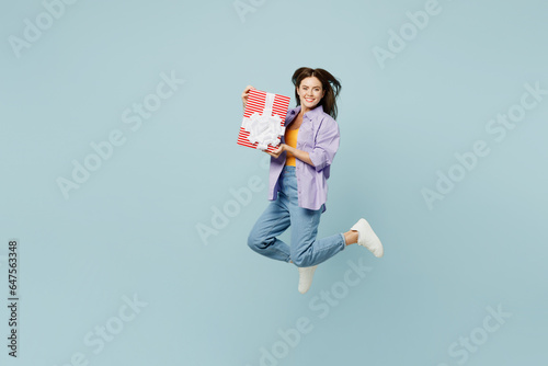 Full body young happy woman she wears purple shirt yellow t-shirt casual clothes jump high hold in hand present box with gift ribbon bow isolated on plain pastel light blue background studio portrait.