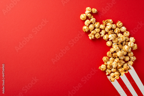 Dynamic top view image of popcorn bursting from a striped container on a red surface, ideal for movie advertising
