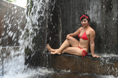 A pretty Asian female in a swimsuit sits  relaxes and shows off her expressions of fun. At a spillway in Thailand.
