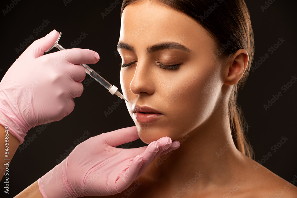 Fototapeta premium Cosmetologist does injections for lips augmentation and anti wrinkle in the nasolabial folds of a beautiful woman. Women's cosmetology in the beauty salon.