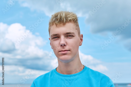 Headshot portrait of handsome smiling teenage guy, blue sky