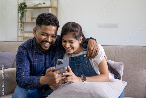 Smiling couple embracing while looking at mobile phone, Loving couple relaxing on sofa