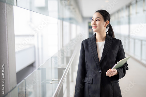 Asian business woman holding a tablet looking away, Fashion business photo of beautiful girl in casual suite with tablet .