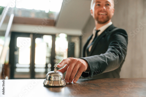 Standing, using hotel desk bell. A man in a black jacket at the hotel reception
